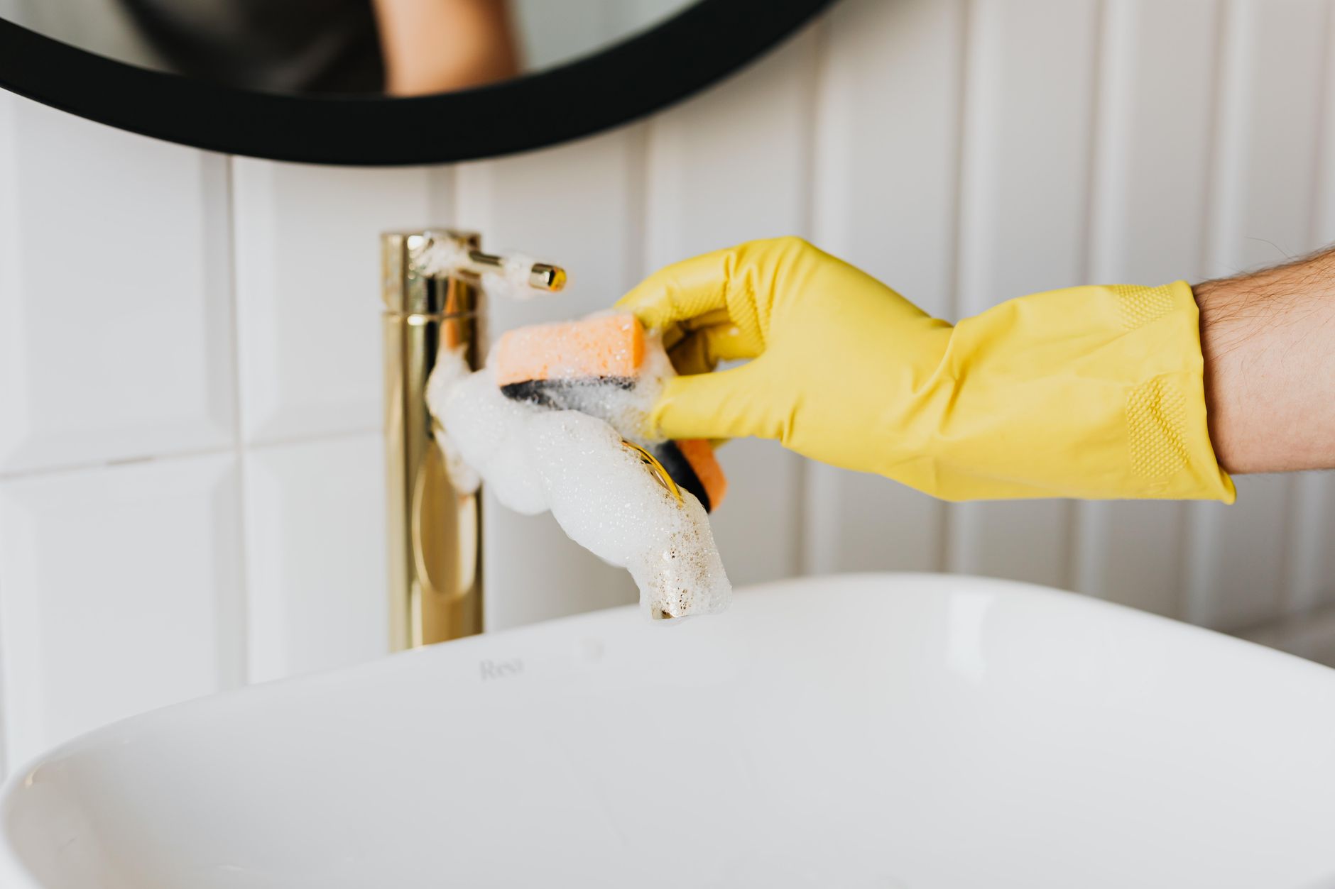 A cleaner wearing gloves scrubbing a bathroom sink